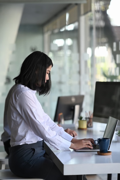 Imprenditrice seduta in un ufficio moderno e digitando i dati sul suo computer portatile per preparare il suo rapporto.