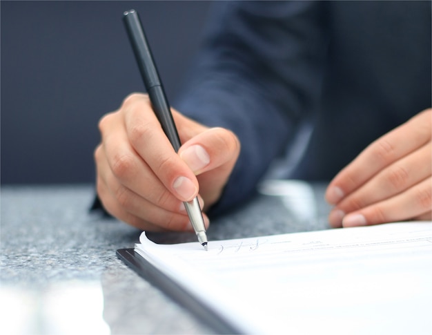 Businesswoman sitting at office desk signing a contract with shallow focus on signature.