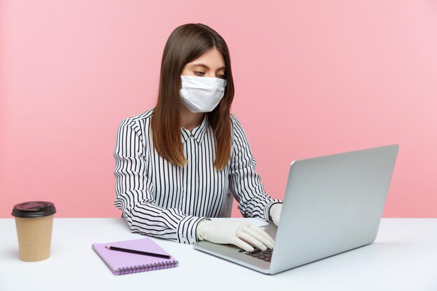 Businesswoman sitting safe healthy with hygienic face mask and protective gloves during quarantine, typing on laptop. Working in self-isolation, coronavirus covid-19 outbreak. indoor, studio shot