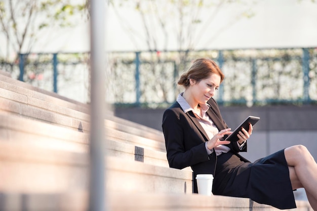 Businesswoman sitting on stairs using tablet