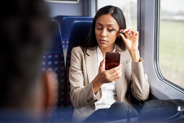 Donna di affari che si siede in treno che va al lavoro mettendo sul trucco