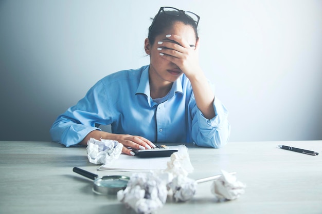 Businesswoman sitting with head in hands at desk covered crumpled papers