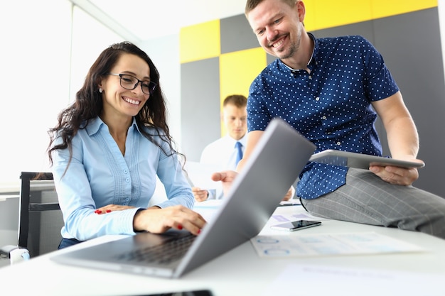 businesswoman smiles and works at laptop next to her colleagues