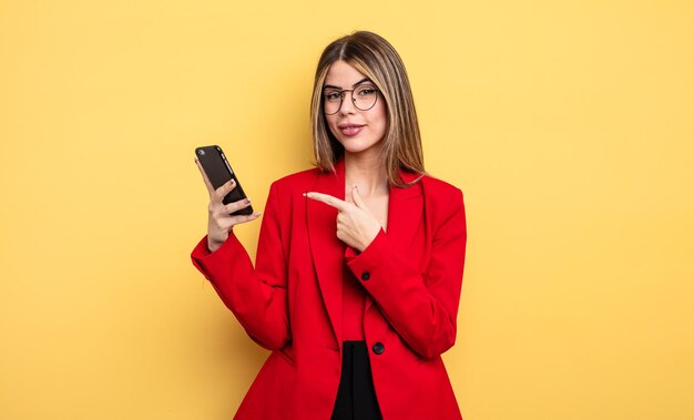 Businesswoman smiling cheerfully feeling happy and pointing to the side smartphone concept