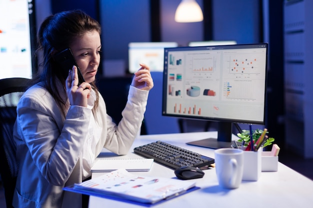 Businesswoman speaking at smartphone with her teamate while working at computer with graphic financial statistics