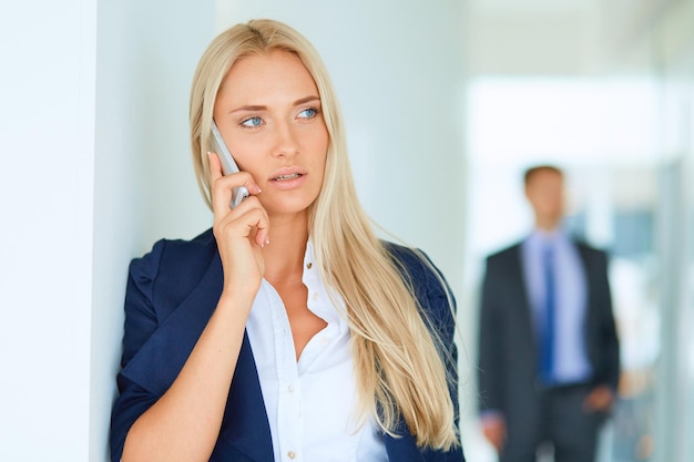 Businesswoman standing against office window talking on mobile phone