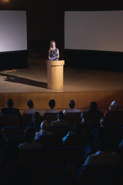Businesswoman standing around podium and giving presentation to the audience