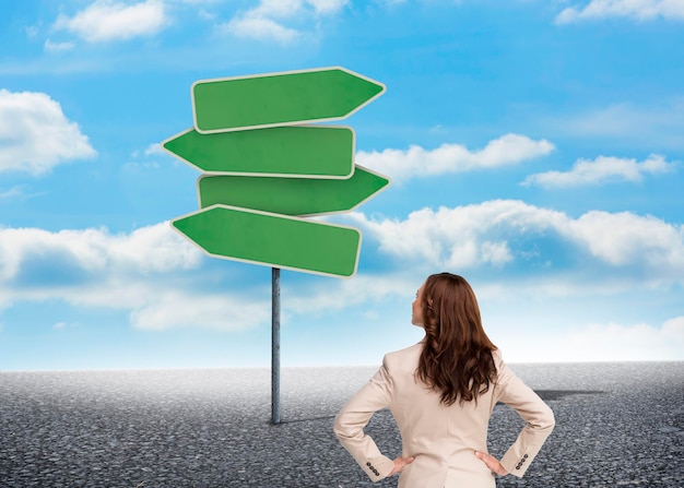 Photo businesswoman standing back to camera looking at road signs