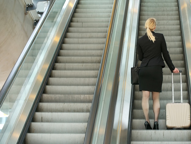 Businesswoman standing on escalator with travel bags