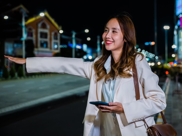 Businesswoman standing hail waving hand taxi on road in busy city street at night