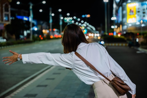 Businesswoman standing hail waving hand taxi on road in busy city street at night