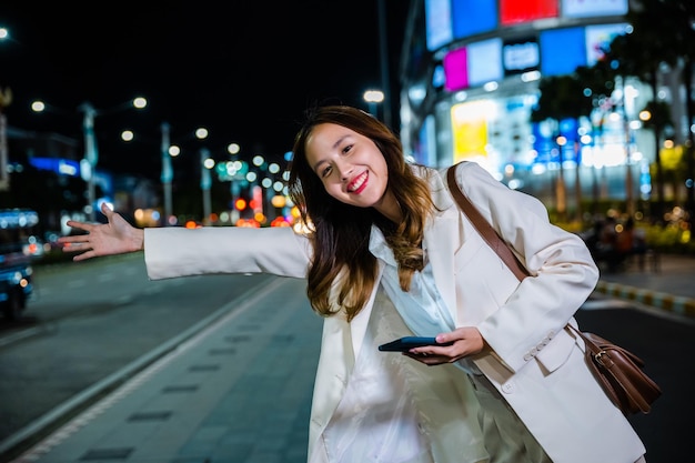 Деловая женщина, стоящая под градом, машет ручным такси на дороге на оживленной городской улице ночью