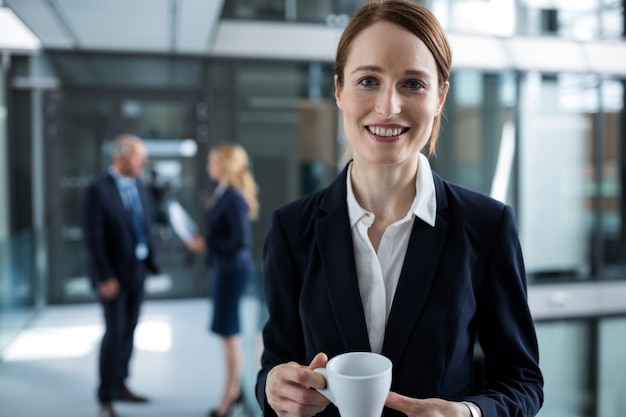 コーヒーカップとオフィスの廊下に立っている女性実業家