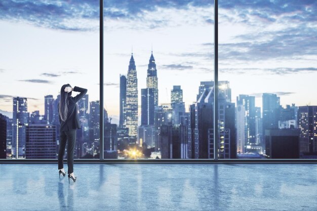 Businesswoman standing thinking in an empty big office room with big windows and night city view Real estate and future success concept