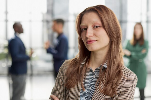 businesswoman standing with her arms crossed in an office while her colleagues have a meeting in the