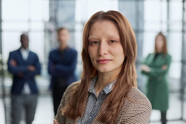businesswoman standing with her arms crossed in an office while her colleagues have a meeting in the