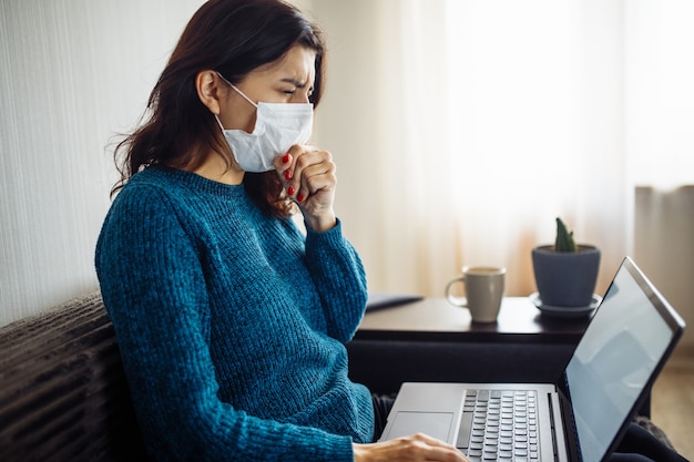 La donna d'affari rimane a casa e lavora durante la quarantena dell'epidemia di coronavirus. lavoratrice che indossa una maschera medica, tossisce e digita su un laptop. concetto di prevenzione della diffusione della pandemia di covid-19.