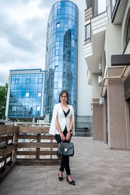 Businesswoman in style suit stands with bag in her hands against of modern office center