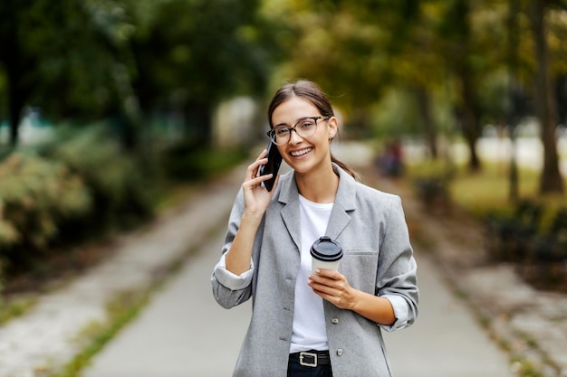 A businesswoman in a suit standing in a park and having a phone call with clients