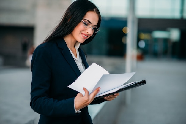 Businesswoman in suit works with notebook outdoor, business center. Modern financial building, cityscape. 