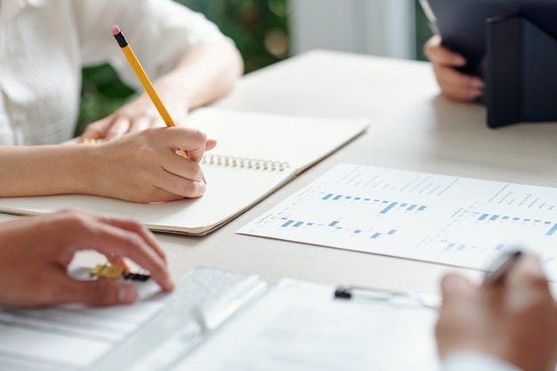 Businesswoman taking notes in planner when having brainstorming session with colleagues