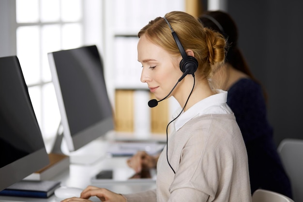 Photo businesswoman talking by headset while sitting in office. call center and diverse people group in business.