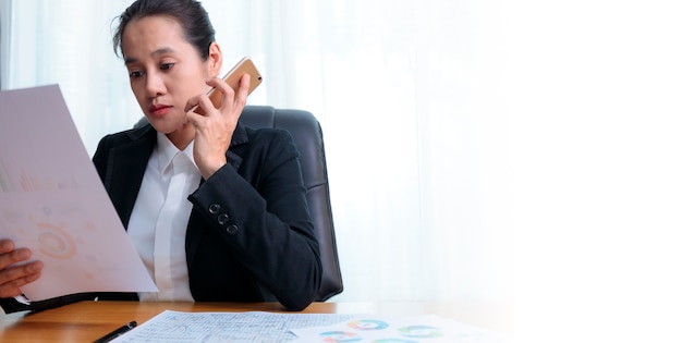 Businesswoman talking by phone at office, looking documents