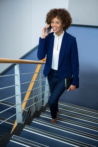 Businesswoman talking on mobile phone while climbing steps at conference centre