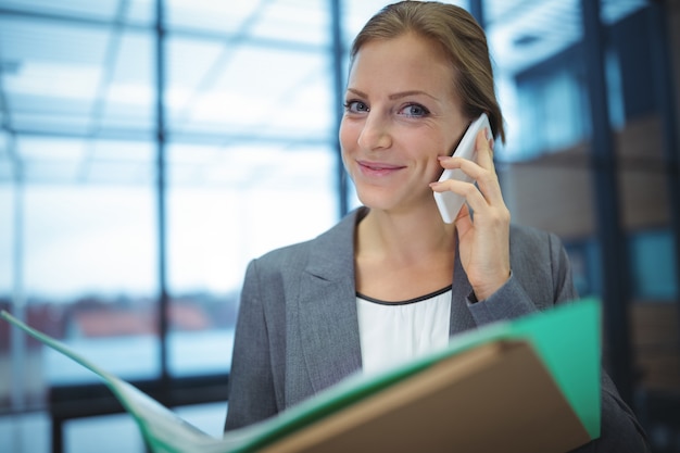 Businesswoman talking on mobile phone while holding files