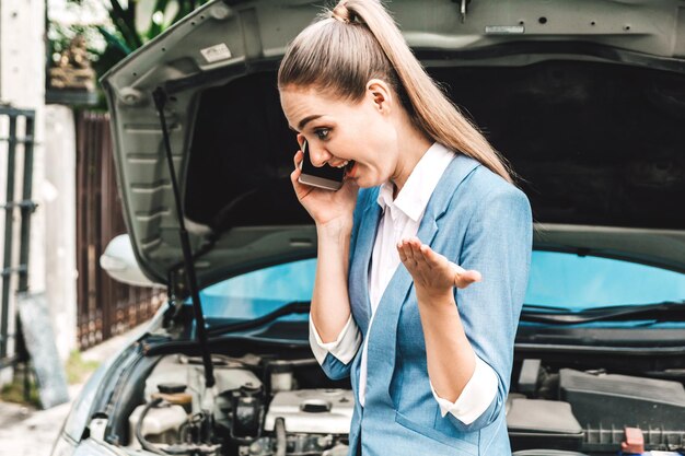 Foto donna d'affari che parla al cellulare mentre si trova accanto a un'auto rotta