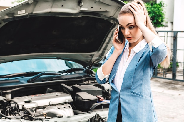 Businesswoman talking on mobile phone while standing by broken car