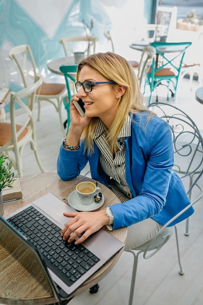 Businesswoman talking on phone and using laptop in a cafe