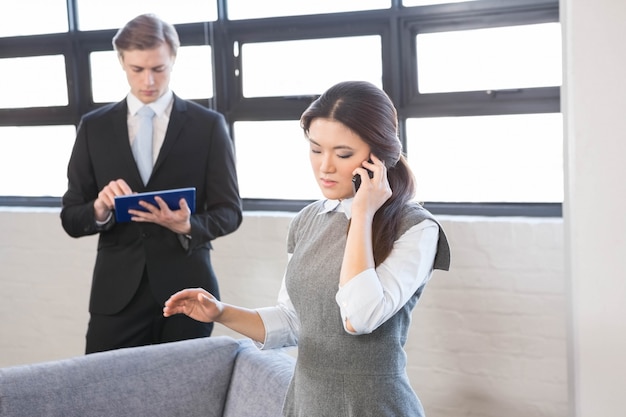 Businesswoman talking on smartphone and businessman using digital tablet in office