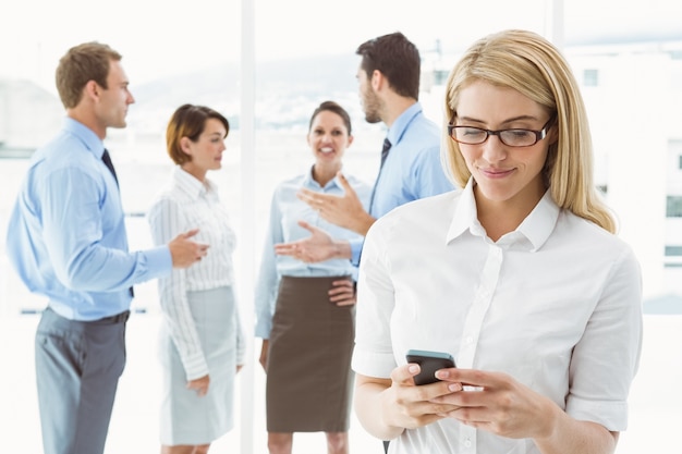 Businesswoman text messaging with colleagues in meeting behind