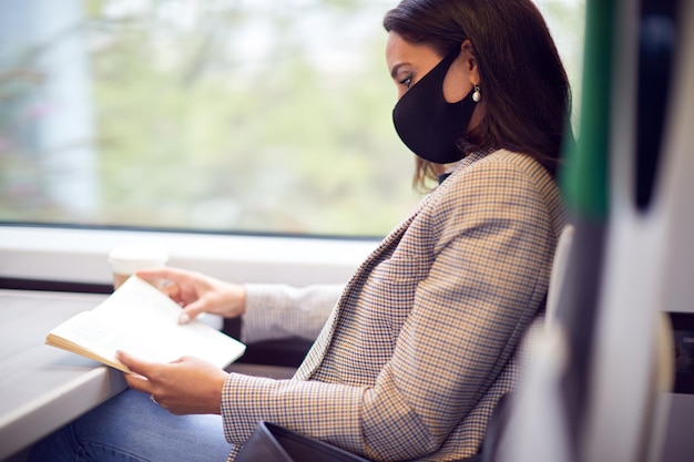 Foto donna d'affari sul treno che si rilassa e legge un libro che indossa una maschera facciale dpi durante la pandemia di salute