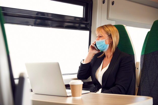 Деловая женщина в поезде работает на ноутбуке в маске для лица во время пандемии