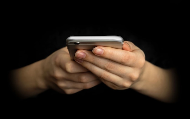 Businesswoman uses mobile phone, front view. Black background, hands and smartphone close-up. High tech, technology and communication concept photo