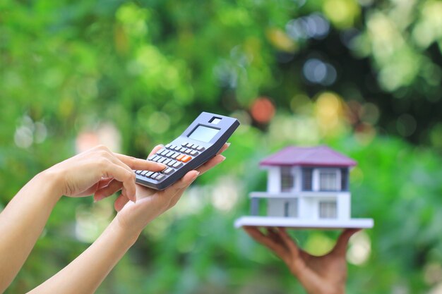 Businesswoman using a calculator and wooden house on green