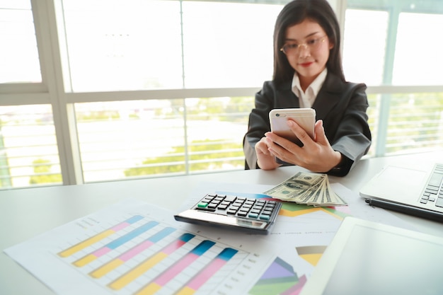 Businesswoman using cell phone and computer while working on  company summary report with graph