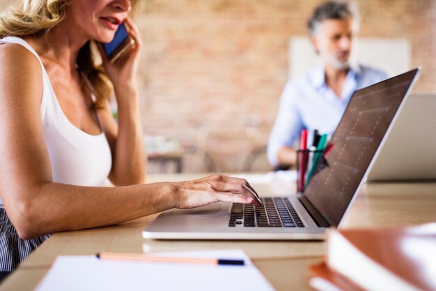 Foto imprenditrice utilizzando il telefono cellulare e il computer portatile alla scrivania in ufficio