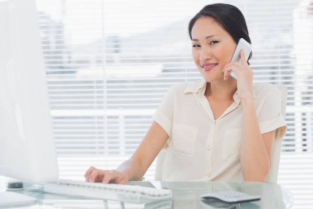 Businesswoman using cellphone and computer at desk