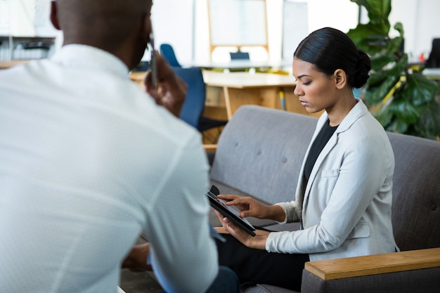 Businesswoman using digital tablet while a colleague talking on mobile phone