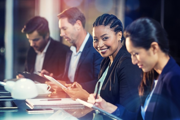 Businesswoman using digital tablet while colleagues writing notes