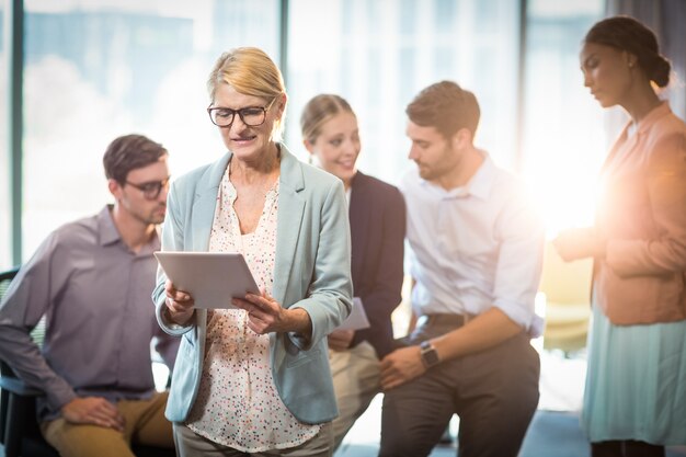 Businesswoman using digital tablet while coworker interacting in the background