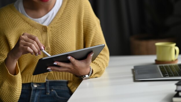 Businesswoman using digital tablet with a stylus pen while sitting in front of laptop