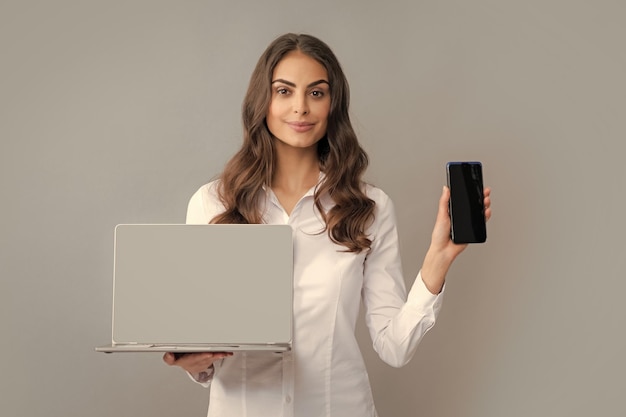 Businesswoman using mobile phone and laptop woman showing empty
laptop screen mock up template with copy space