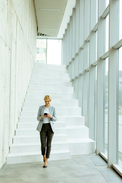 Businesswoman using mobile phone on modern office hallway