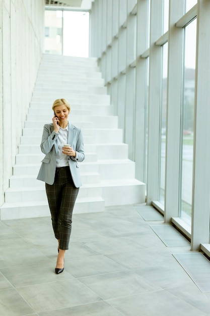 Businesswoman using mobile phone on modern office hallway