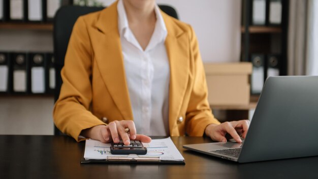 Деловая женщина, использующая мобильный телефон, планшетный ноутбук и калькулятор в офисе