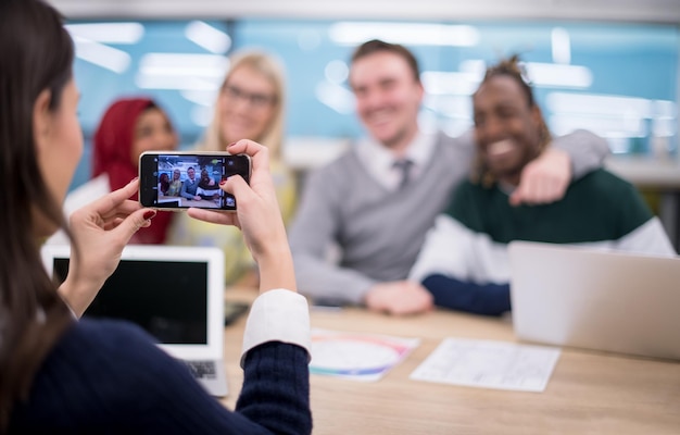 businesswoman using mobile phone for taking photo of her multiethnic business team at modern startup office